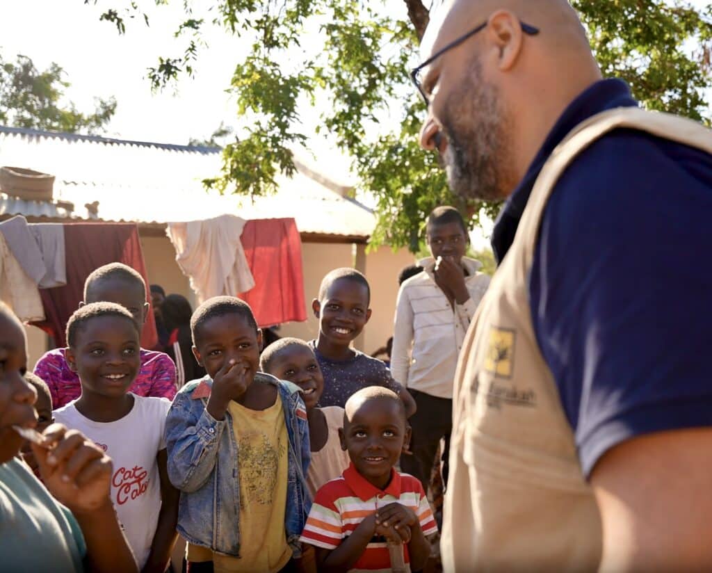 Un travailleur humanitaire souriant de l'association Barakah échange avec un groupe d'enfants orphelins dans un village africain.