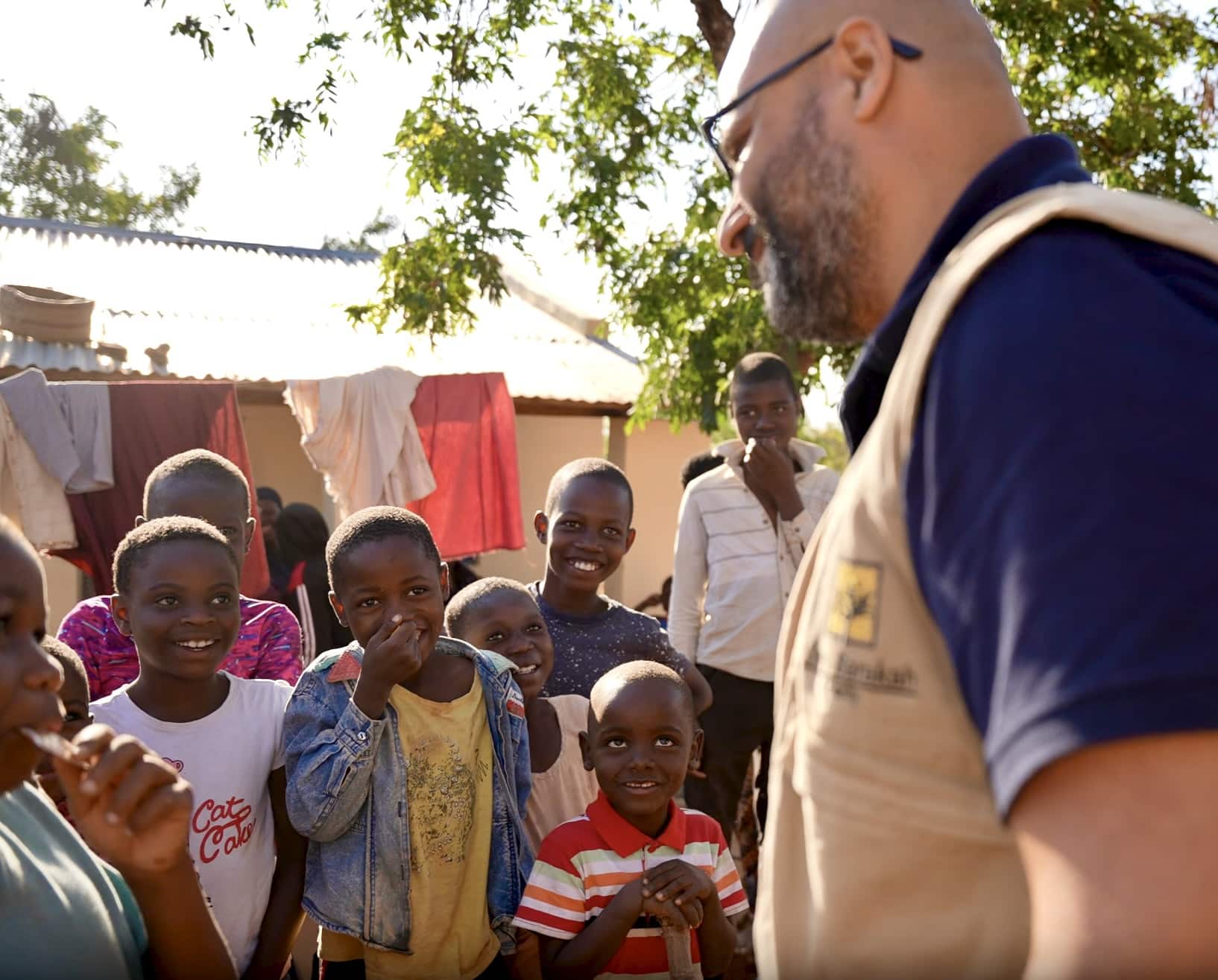 Un travailleur humanitaire souriant de l'association Barakah échange avec un groupe d'enfants orphelins dans un village africain.