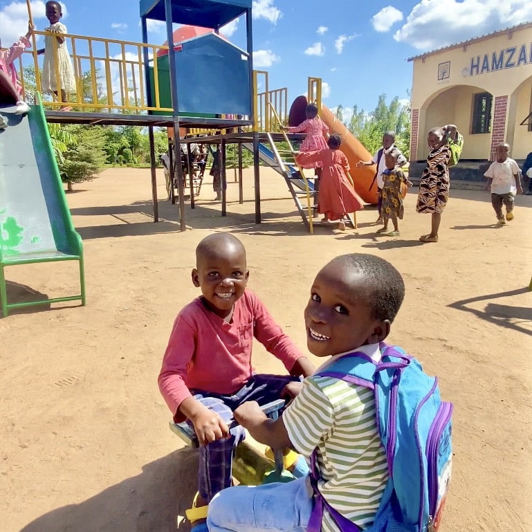 Orphan children play safely on the seesaw and slides in an outdoor playground.