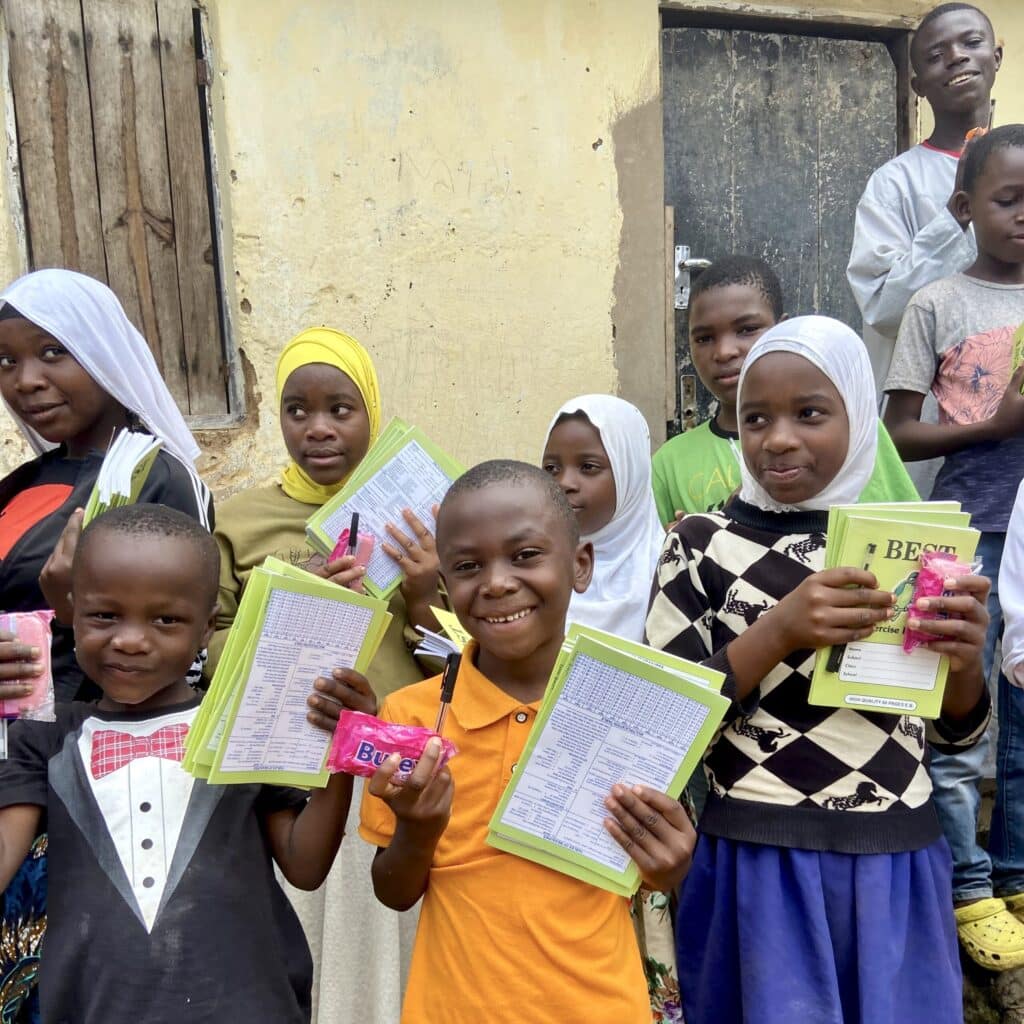 A group of orphan children smile while showing their new notebooks and school supplies received in an African village.
